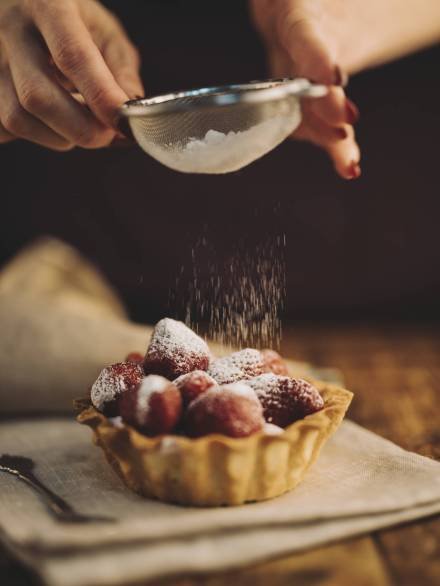 close-up-woman-dusting-sugar-powder-strawberry-tart